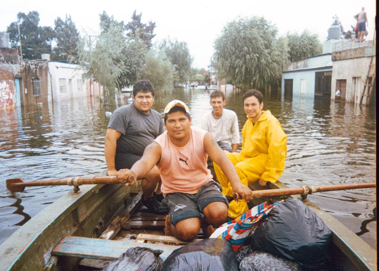 Imagen de cuatro hombres jóvenes en un bote de remo realizando la entrega de provisiones en el Barrio Santa Rosa de Lima, Santa Fe